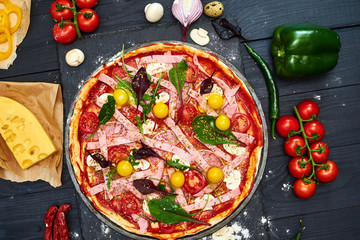 Raw pizza with mozzarella cheese, meat, tomatoes, mushrooms, peppers, herbs on a dark wooden background. Cooking delicious italian pizza.