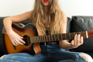 Crop view of young woman sitting on couch playing guitar