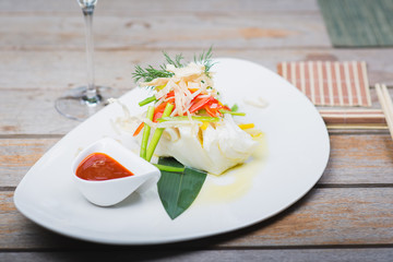 White fish seabass fillet with vegetables and white wine on a wooden table in a restaurant with decor. Tasty and healthy food. A cozy evening in a restaurant during a date. Beautiful table setting.