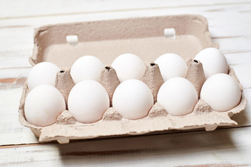 White chicken eggs in a tray on a light wooden background.