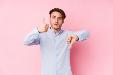 Young caucasian man posing in a pink background isolated showing thumbs up and thumbs down, difficult choose concept