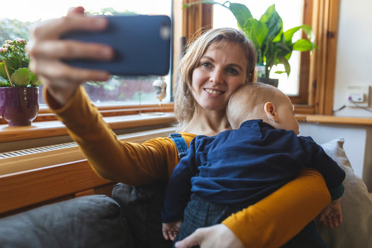 Woman taking a selfie with her cute sleeping son on the sofa