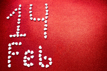 February 14 inscription of white candy hearts on a dark red background with sequins with space for text