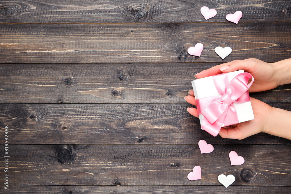 Wall mural Female hands holding gift box with ribbon and hearts on brown wooden table