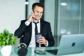 Smiling man talking on mobile phone while using laptop computer at desk.