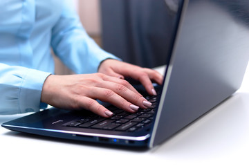 young woman in a blue shirt at a white table works in the office with a laptop