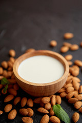 Fresh almond milk in wooden bowl and almonds on black stone background