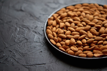 Whole almond nuts in black plate placed on black stone table