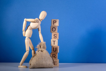 Wooden mannequin with a bag near the tower of cubes with the inscription Posture.