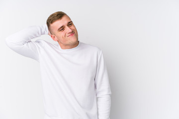 Young caucasian man on white background touching back of head, thinking and making a choice.