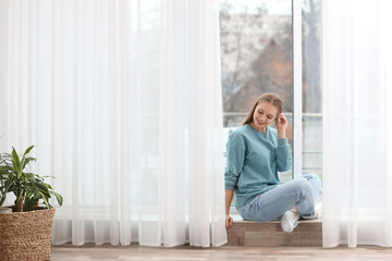 Beautiful young woman near window at home