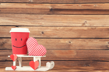 Fabric heart with paper cup and white sleigh on brown wooden table