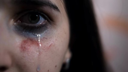 Close-up of the eye of a young female victim of domestic violence. A tear runs down. Signs of a beating.