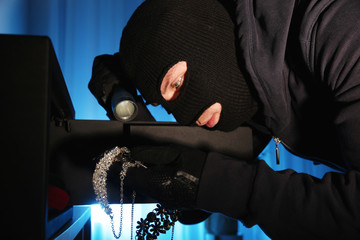 Thief taking jewelry out of steel safe indoors at night