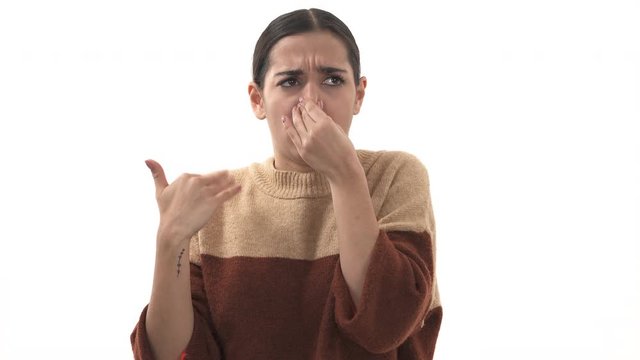 Close-up portrait of young woman, disgust on face, pinches nose, looks funny. Something stinks, very bad smell, situation. Negative emotion, facial expression