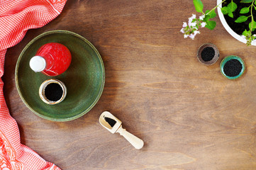 Glass bottle of strawberry juice with Basil seeds. A ceramic plate with gravy boats and a scoop of Basil seeds, a linen towel and a pot of blooming flowers. Top view, horizontal position, copy space..