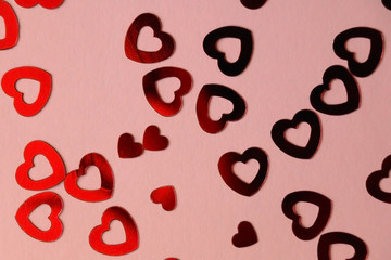 Red heart shaped confetti on pale pink background. Love and valentine concept. Top view.