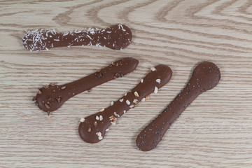 Four milk chocolates with coconut and hazelnut pieces on wooden background