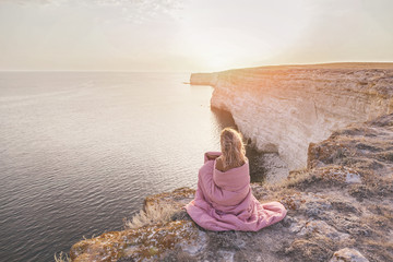 Woman covered in bed duvet relaxing and watching sea landscape on sunset