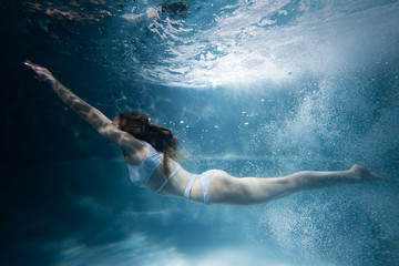 Fototapeta na wymiar Woman dives under water among the rays of light and air bubbles