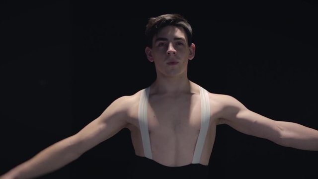 Professional Caucasian male ballet dancer spinning and smiling in darkness. Handsome confident man dancing classic dance. Choreography, elegance, art. Slowmo.