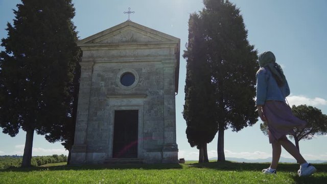 Low angle view of woman in headscarf going to chapel on sunny day. Long shot