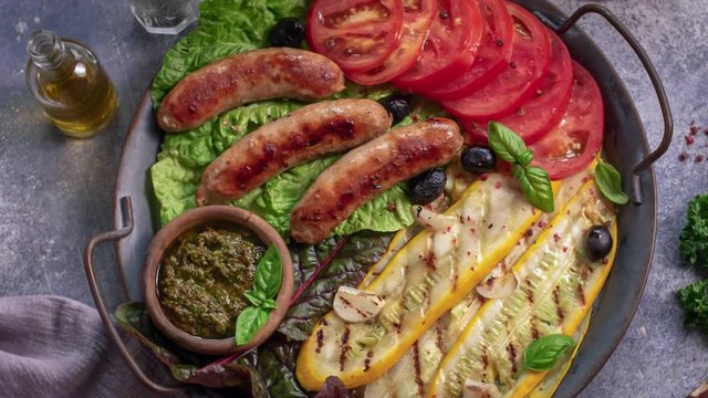 Roasted sausages with grilled courgette and tomatoes on metal tray rotation