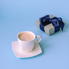 Cup of coffee and gift in a box on classic blue background. Valentines day, birthday or Womens day concept.