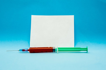 Syringe with blood on a blue background with a white piece of paper copy space