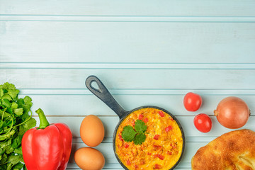 Flatlay on a blue background background. Omelet with tomatoes, onions and peppers, Menemen. Healthy breakfast. Photo with copy space.
