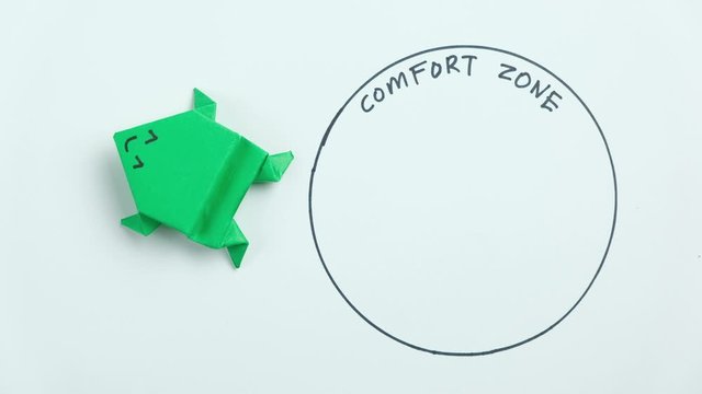 Step out from the comfort zone concept. A dark green origami frog jumping out of the comfort zone.