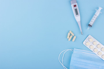 Concept image of four yellow capsule, electronic thermometer, medical mask, syringe on a blue background. Flat lay, copy space. Medicine concept seasonal illness flu, virus, runny nose, temperature.