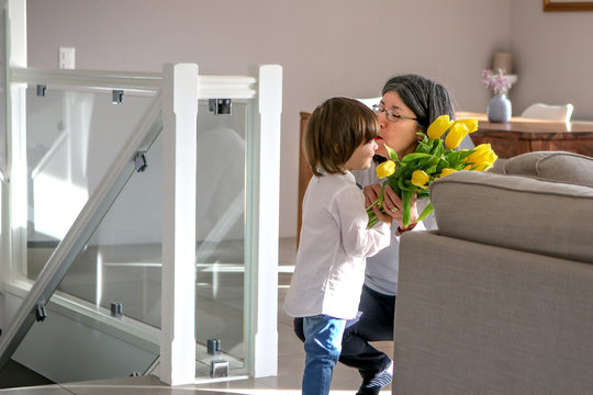 Happy women&acirc;&euro;&trade;s day. Little child hugging his grandmother to greet her with bouquet of tulip flowers in her house. Grandparents day. Focus on woman.