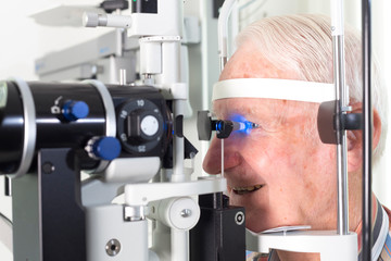 Optometry Concept - senior man having his eyes examined by an eye doctor