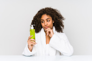 Young african american woman holding an aloe vera looking sideways with doubtful and skeptical...