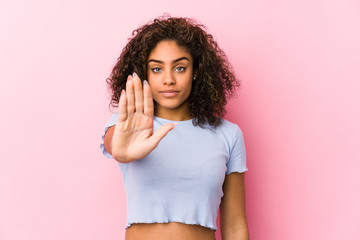 Young african american woman against a pink background standing with outstretched hand showing stop sign, preventing you. - obrazy, fototapety, plakaty
