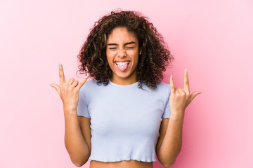 Young african american woman against a pink background showing rock gesture with fingers