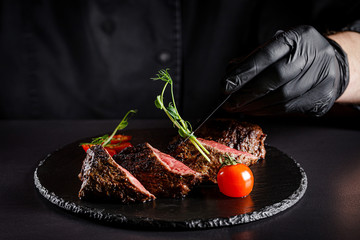 The concept of cooking meat. The chef cook decorates a meat dish on a black background, a place...