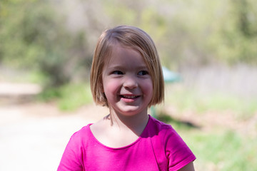 Smiling, excited little girl in a pink dress playing outside