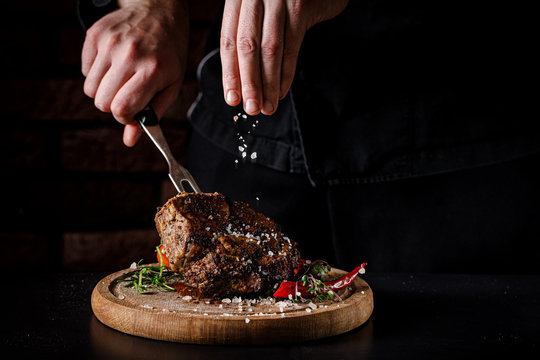 The concept of cooking meat. The chef cook salt on the cooked steak on a black background, a place under the logo for the restaurant menu. food background image, copy space text