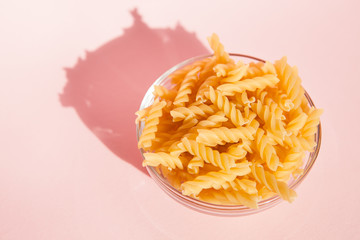 Italian rotini pasta in glass bowl from top view on pink background