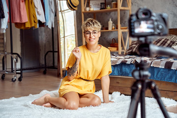 Blogger. Young woman in glasses sitting at stylish apartment recording video on camera telling tips happy