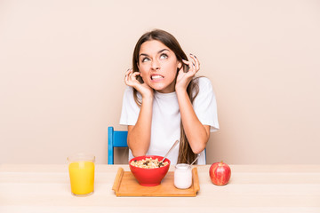 Young caucasian woman having a breakfast isolated covering ears with hands.