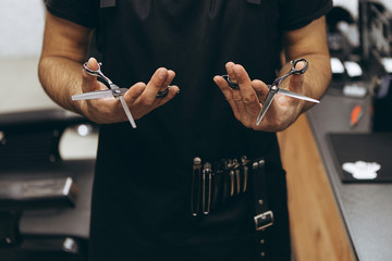 professional barber tool: sharpened scissors held by a haircut master in a modern barber shop. A...