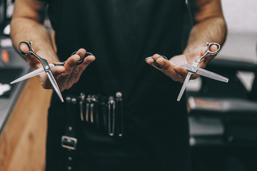 professional barber tool: sharpened scissors held by a haircut master in a modern barber shop. A concept for barbershops, beauty salons and hairdressers