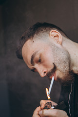 Fototapeta premium portrait of a young stylish bearded man with a cigarette in his hands: not a healthy lifestyle, smoking, bad habits and nicotine addiction