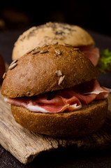 Delicious crispy burger bun with sliced ham on a vintage wooden cutting board. Dark moody food still life.