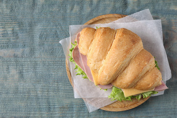 Tasty croissant sandwich with ham on light blue wooden table, top view