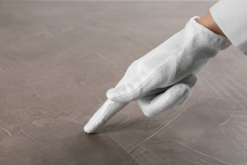 Person in white glove checking cleanliness of beige stone table, closeup