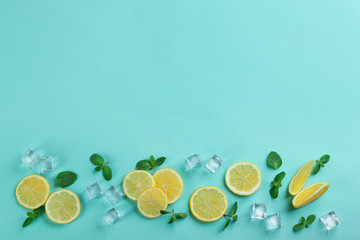 Lemonade layout with juicy lemon slices, mint and ice cubes on turquoise background, top view. Space for text